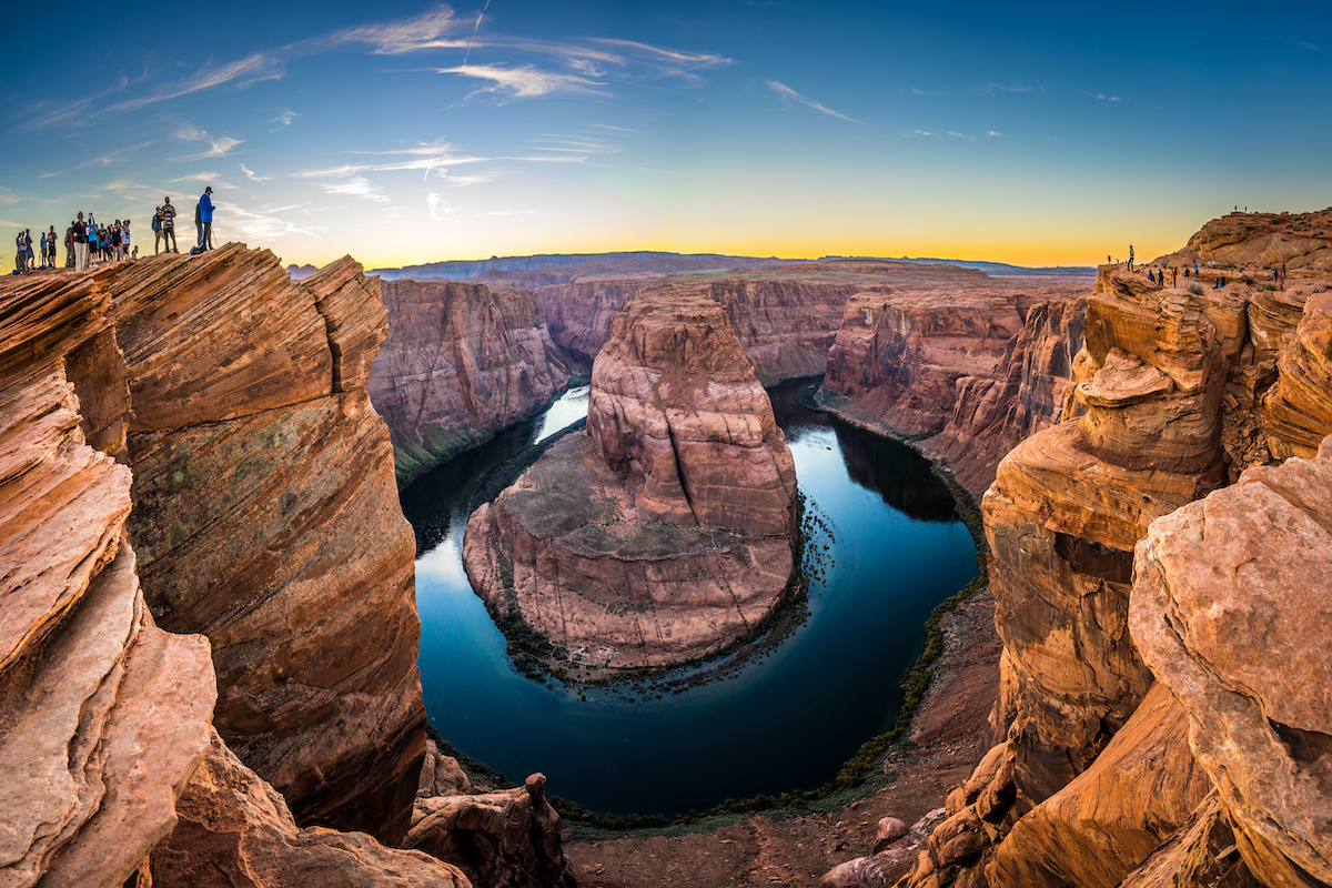 Due miliardi di anni nella roccia! Tutto sul Grand Canyon, dalla storia alle curiosità 

 

Sai che affacciarti sul bordo del Grand Canyon significa avere davanti agli occhi quasi due miliardi di anni di storia della Terra? Il Grand Canyon e la sua storia non cominciano con l'uomo, cominciano con l'acqua.  

 

Circa sei milioni di anni fa il fiume Colorado ha iniziato a incidere l'altopiano dell'Arizona settentrionale e, scendendo, ha riportato alla luce strati di roccia sempre più antichi, fino a quelli formatisi quasi due miliardi di anni fa. Il risultato è una gola lunga 446 chilometri, profonda fino a 1.857 metri e larga da 500 metri a 29 chilometri. 

 

I numeri, però, raccontano solo metà del viaggio. L'altra metà appartiene a chi in questa gola vive da almeno diecimila anni, a chi ci è arrivato per caso cercando tutt'altro e a chi si è battuto perché restasse così com'è. 

 

Nei prossimi paragrafi ripercorreremo insieme la storia di questa splendida gola, e ti sveleremo cinque curiosità da conoscere prima di partire. 

 

Come si è formato il Grand Canyon? La sua storia 

 

 

 

Il canyon si apre nell'angolo sud-occidentale del Colorado Plateau, l'altopiano che attraversa Arizona, Utah, Colorado e Nuovo Messico. La sua forma nasce da due movimenti opposti, la terra che si solleva e il fiume che scava. 

 

Il sollevamento viene prima. Circa 75 milioni di anni fa la stessa spinta che ha costruito le Montagne Rocciose ha alzato l'altopiano di alcuni chilometri, dando al Colorado la pendenza per incidere la roccia. Il fiume, però, non taglia la pietra da solo. Durante le piene trascina massi e ghiaia sul fondo, ed è quel materiale a lavorare come uno scalpello. 

 

Quanti anni ha allora? I geologi ne discutono ancora. Uno studio pubblicato su Nature Geoscience nel 2014 ha mostrato che alcuni tratti erano già incisi oltre 50 milioni di anni fa, mentre i due segmenti decisivi si sono formati meno di sei milioni di anni fa. 

 

Comunque sia andata, il risultato si legge come un libro sfogliato al contrario. Più si scende, più si va indietro nel tempo. Procedendo in questo senso, gli strati che si incontrano sono: 

 

gli strati sedimentari superiori. Calcari, arenarie e argilliti depositati nel corso del Paleozoico da mari poco profondi, dune desertiche e paludi costiere; 

la Great Unconformity. Un contatto netto tra rocce di età molto diverse, dove manca all'appello un lunghissimo capitolo geologico. È uno degli enigmi più studiati al mondo; 

le rocce del basamento. Sul fondo, vicino al fiume, gli scisti e i graniti più antichi del canyon, formatisi quasi due miliardi di anni fa. 

 

I colori che si vedono dal bordo, dal rosso all’ocra e al grigio dipendono dalla composizione di questi strati e dal ferro che li attraversa. Cambiano con la luce, e per questo il canyon delle otto del mattino non è il canyon delle sei di sera. 

 

Lo stesso sollevamento dell'altopiano che ha permesso al Colorado di lavorare così in profondità ha modellato, poco più a nord, gli archi naturali dello Utah e le guglie che si incontrano lungo i sentieri del Bryce Canyon. La roccia, però, è solo il primo capitolo. 

 

Chi ha scoperto il Grand Canyon? Dai nativi americani a John Wesley Powell 

 

 

 

Quando si parla del Grand Canyon e della sua storia, la domanda su chi lo abbia scoperto ha una risposta scomoda: nessuno lo ha scoperto, perché qualcuno c'era già. Le persone abitano questa gola da più di diecimila anni. Oggi, infatti, il National Park Service riconosce 11 tribù tradizionalmente associate al Grand Canyon, tra cui Havasupai, Hualapai, Hopi, Navajo, Zuni, la Yavapai-Apache Nation e diverse bande Paiute. Qui hanno coltivato, cacciato, costruito villaggi e tramandato racconti, e qui continuano a vivere. 

 

Il primo europeo ad affacciarsi sul canyon fu lo spagnolo García López de Cárdenas, nel 1540. Faceva parte della spedizione di Coronado e cercava il grande fiume di cui parlavano gli Hopi. Trovò un ostacolo, non una meraviglia, e dopo di lui la gola rimase quasi ignorata per tre secoli. 

 

Il vero cambio di sguardo arriva nel 1869 con John Wesley Powell, maggiore e geologo, veterano della Guerra Civile. Con quattro barche e nove uomini scese il fiume Colorado attraverso il canyon: fu la prima spedizione documentata a percorrerlo per intero. Powell descrisse le rocce esposte come le "pagine di un grande libro di storia", e fu lui a diffondere il nome con cui oggi lo conosciamo. 

 

La sua impresa aprì la strada a geologi, fotografi e infine viaggiatori. Fu il momento in cui il canyon smise di essere un problema da aggirare e cominciò a essere un luogo da attraversare, lo stesso passaggio che, in altri territori del West, ha segnato i luoghi della storia dei nativi americani. 

 

Dal 1893 al parco nazionale, storia del Grand Canyon e della sua tutela 

 

 

 

Diventare parco nazionale non fu né rapido né scontato. Per decenni la gola interessò soprattutto i cercatori di rame e uranio, e le compagnie minerarie fecero muro contro ogni ipotesi di protezione integrale. 

 

Theodore Roosevelt la visitò nel 1903 e ne uscì convinto: quel paesaggio andava lasciato com'era. Usò l'Antiquities Act per dichiararlo monumento nazionale nel 1908, ma servirono ancora undici anni prima che il Congresso lo trasformasse in parco. 

 

Il 26 febbraio 1919 il presidente Woodrow Wilson firmò il Grand Canyon National Park Act, trasformando il canyon nel diciassettesimo parco nazionale degli Stati Uniti.   

 

Da allora il perimetro si è ampliato e il riconoscimento è cresciuto. Oggi il parco supera i 4.900 chilometri quadrati e nel 2024 ha accolto 4.919.163 visitatori: resta il cuore di ogni itinerario tra i grandi parchi americani. 

 

5 curiosità sul Grand Canyon da conoscere prima di partire 

 

 

 

Conoscere la storia del Grand Canyon è importante, ma alcune cose si capiscono solo quando qualcuno te le racconta sul posto. Sono i dettagli che raramente si trovano nelle guide e che, una volta noti, cambiano quello che vedi dal bordo: un nome, una data, un vuoto tra due strati di roccia. Ecco, allora, 5 curiosità che vale la pena di conoscere prima di partire. 
 

Non è il canyon più profondo del mondo. Altre gole scendono più in basso: il primato del Grand Canyon sta nell'insieme di lunghezza, larghezza e profondità, non in un singolo record. 

I due bordi sono due mondi diversi. Il South Rim, intorno ai 2.100 metri, è il più accessibile e aperto tutto l'anno. Il North Rim supera i 2.400 metri, è più fresco, molto meno frequentato e chiude nei mesi invernali per la neve. 

Il capitolo che manca. Lungo la Great Unconformity due strati che si toccano sono separati da un abisso di tempo: geologi da tutto il mondo continuano a studiare dove sia finita la roccia mancante. 

A dare i nomi fu un uomo con un braccio solo. Powell aveva perso il braccio destro nella battaglia di Shiloh. Molti punti panoramici del bordo sud portano invece i nomi delle tribù native: Hopi Point, Navajo Point, Yavapai Point, Mohave Point. 

Un nome restituito. Nel 2023 l'oasi lungo il Bright Angel Trail, per decenni chiamata Indian Garden, è tornata a chiamarsi Havasupai Gardens, su richiesta della tribù che vi coltivava fino agli anni Venti. 

 

Dal bordo sud tutto questo si legge in un colpo d'occhio, e ogni affaccio ha la propria luce e la propria ora: i punti panoramici del Grand Canyon meritano tempo, non fretta.  

 

In viaggio nel Grand Canyon con Utat: due itinerari per viverlo 

 

 

Leggere curiosità sul Grand Canyon, la storia e la sua formazione geologica è una cosa. Sentirla sotto i piedi, con qualcuno accanto che sa spiegarti cosa stai guardando, è un'altra. Noi di UTAT accompagniamo i viaggiatori negli Stati Uniti da oltre novant'anni e conosciamo direttamente i luoghi che proponiamo.  

 

Nel nostro catalogo il canyon è tappa di due itinerari pensati per esigenze diverse: 

 

Golden West USA — quattordici giorni da Los Angeles a San Francisco. Oltre al Grand Canyon si attraversano Antelope Canyon, la Monument Valley con jeep tour condotto dai Navajo, Arches, Canyonlands, Bryce, la Death Valley e Yosemite; 

 

Parks Explorer — nove giorni e dieci parchi nazionali, da Los Angeles a Las Vegas. Una formula più compatta, per chi vuole concentrare in un solo viaggio Grand Canyon, Mesa Verde, Canyonlands e Zion. 

 

Se hai dubbi su quale dei due somigli di più al viaggio che hai in mente, contattaci: ne parliamo insieme e scegliamo il periodo giusto per partire. 

 

Glossario per il tuo viaggio 

 

Colorado Plateau. Vasto altopiano tra Arizona, Utah, Colorado e Nuovo Messico. Il suo lento sollevamento ha permesso al fiume di scavare tanto in profondità. 

South Rim. Il bordo meridionale del canyon, intorno ai 2.100 metri di quota: il più accessibile, servito e visitato, aperto tutto l'anno. 

North Rim. Il bordo settentrionale, oltre i 2.400 metri: più fresco e più appartato, chiuso ai visitatori nei mesi invernali. 

Great Unconformity. Il contatto tra rocce di età molto distanti visibile lungo le pareti, dove manca un lunghissimo intervallo di tempo geologico. 

Antiquities Act. Legge statunitense del 1906 che consente al Presidente di istituire monumenti nazionali senza passare dal Congresso. 